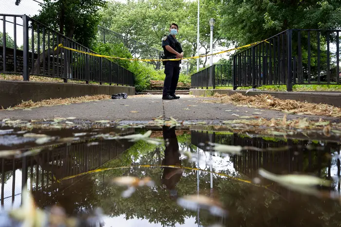 A New York City police officer stands guard on July 7th, 2020 at the scene where a 27-year-old man was found shot to death in a park in Crown Heights.